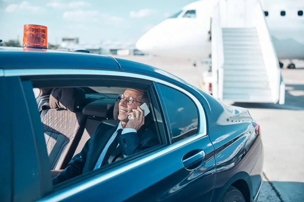 Businessman with a suitcase walking towards a luxury car at Philadelphia International Airport, Pennsylvania, ready for a smooth airport transfer with Philadelphia Car and Limo service