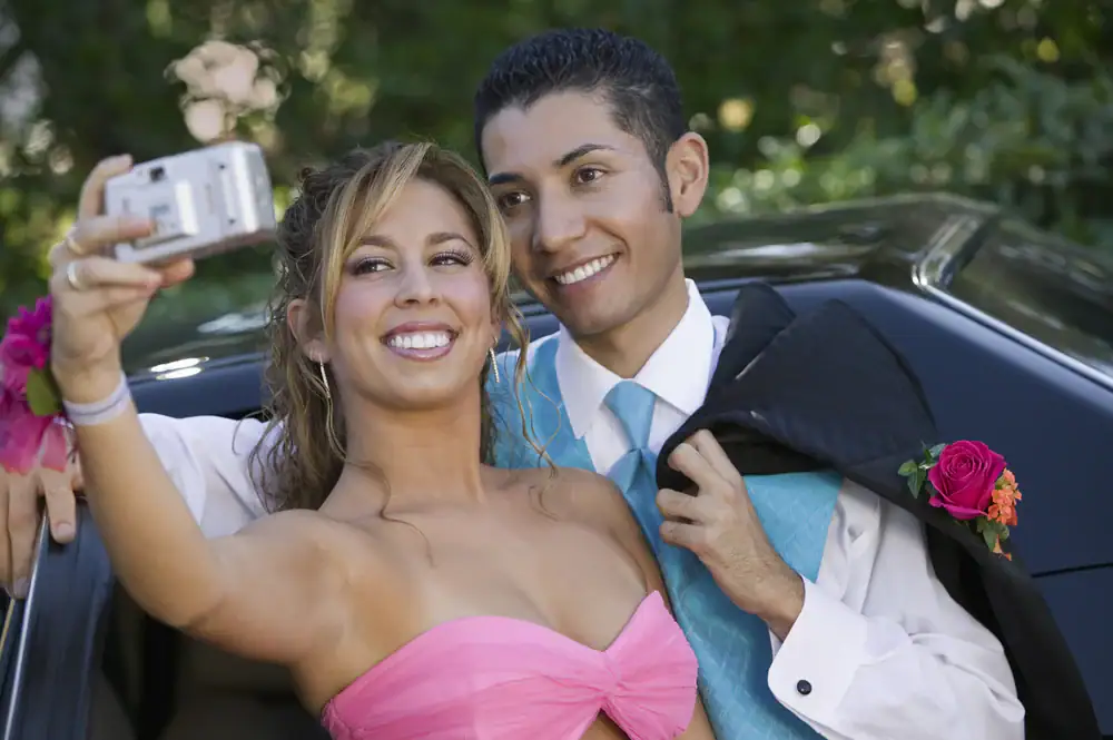 A prom couple taking a selfie outside a luxurious limo in Philadelphia, capturing the excitement of the night with the city's skyline in the background